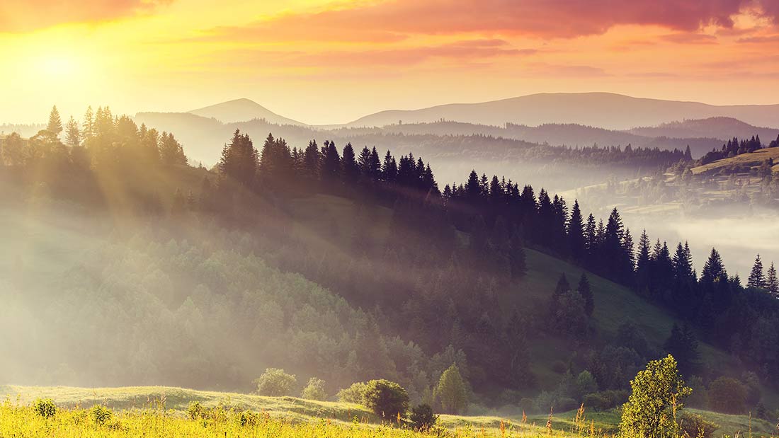 A beautiful sunset over the mountains with trees in the foreground.
