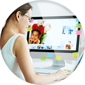 A woman sitting at her computer with post it notes on the wall.
